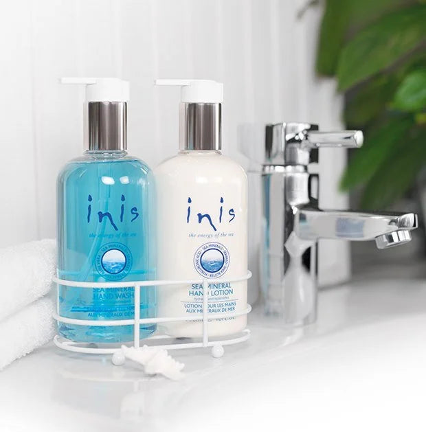 Inis hand wash and sea mineral hand lotion in a white wire caddy beside a bathroom sink
